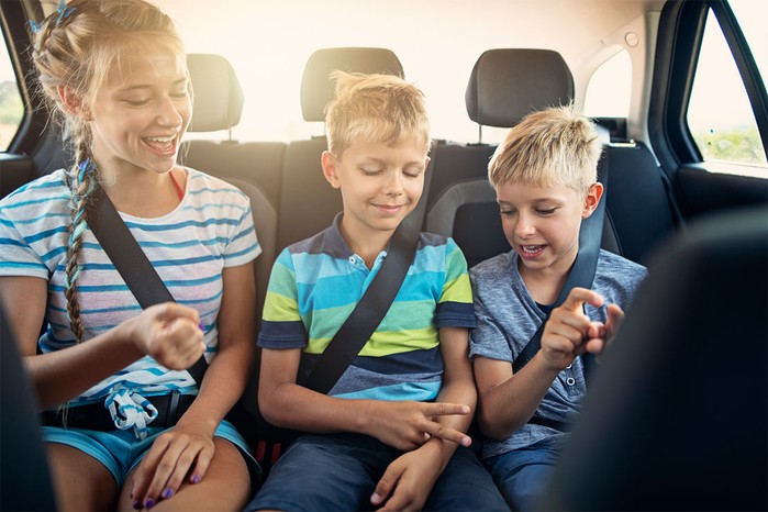 2 boys and a girl in back seat of car playing rock paper scissors